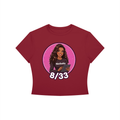 A maroon short-sleeve crop top t-shirt featuring a circular graphic of a woman with the text 'Ninibaby' and '8/33' printed on the front, displayed against a solid white background.
