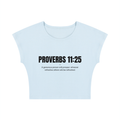 A light blue cropped t-shirt with black text on the front reading 'PROVERBS 11:25' and a smaller quote underneath, displayed on a solid white background.
