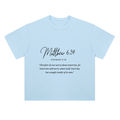 A light blue short-sleeve t-shirt with a black printed Bible verse from Matthew 6:34 on the chest, displayed flat against a solid white background.